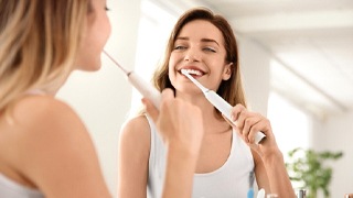 Young woman in white shirt using electric toothbrush