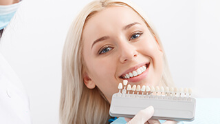 Woman in dental chair comparing teeth to shade chart