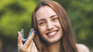 Happy woman holding aligner for SureSmile orthodontic treatment