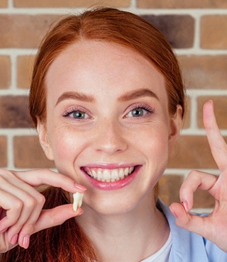 Happy woman holding tooth after tooth extraction in Lakeville