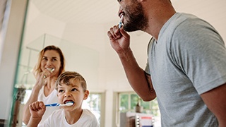 Man, woman, and boy brushing their teeth together in front of mirror