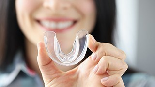 Woman holding transparent mouthguard towards camera