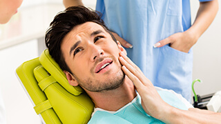 Man in dental chair holding cheek in pain
