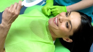 Dental patient using mirror to admire results of cosmetic treatment