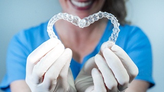 dental professional holding up clear aligners in heart shape