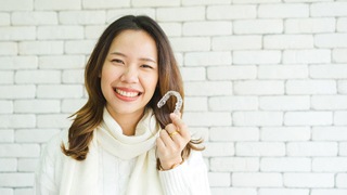 woman in white sweater smiling and holding up SureSmile Aligner