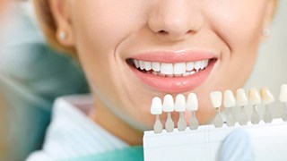 Gloved hand holding shade guide next to patient’s teeth