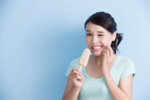 Woman grimacing due to sensitive teeth as she eats ice cream