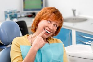 Happy patient pointing at her dental implants after tooth extraction