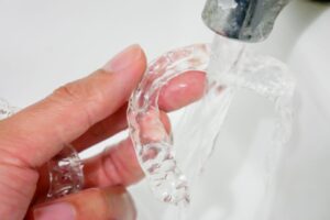 Person rinsing clear aligners under tap water